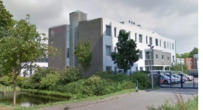 Modern kantoorgebouw aan de Van Bleyswijckstraat met omheind parkeerterrein en omliggend groen.